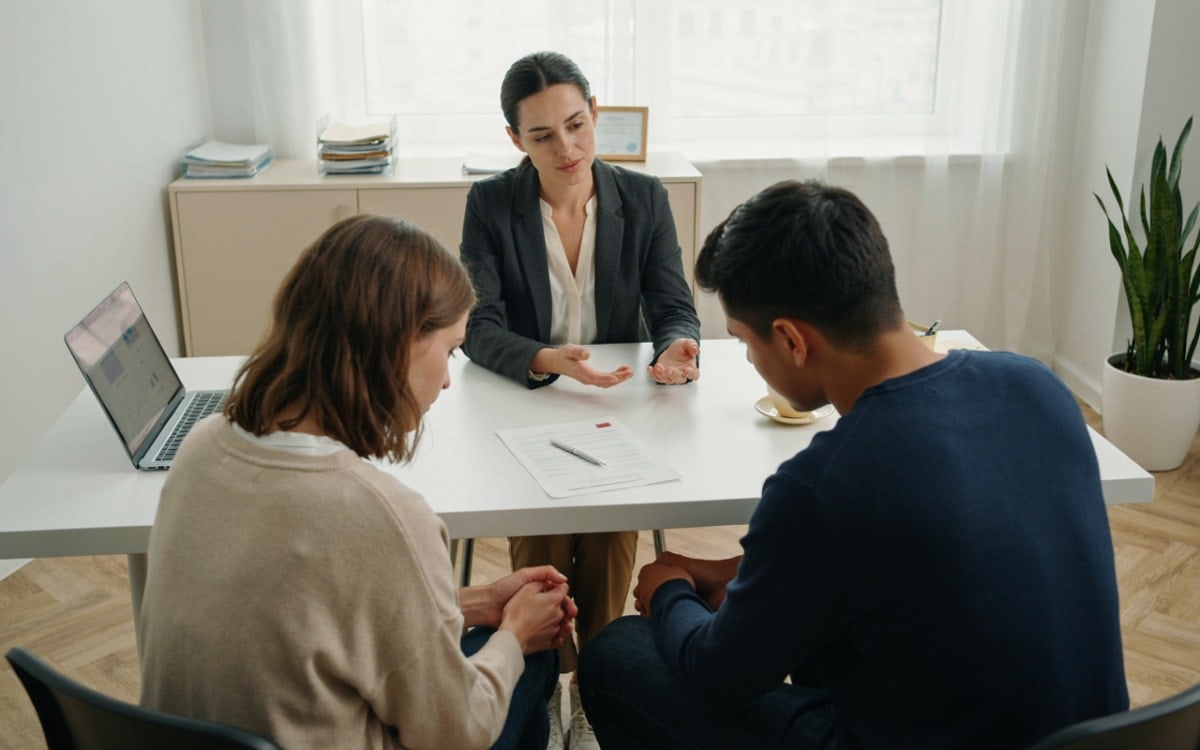 Casal conversa com uma profissional do mercado imobiliário em uma mesa de escritório iluminada